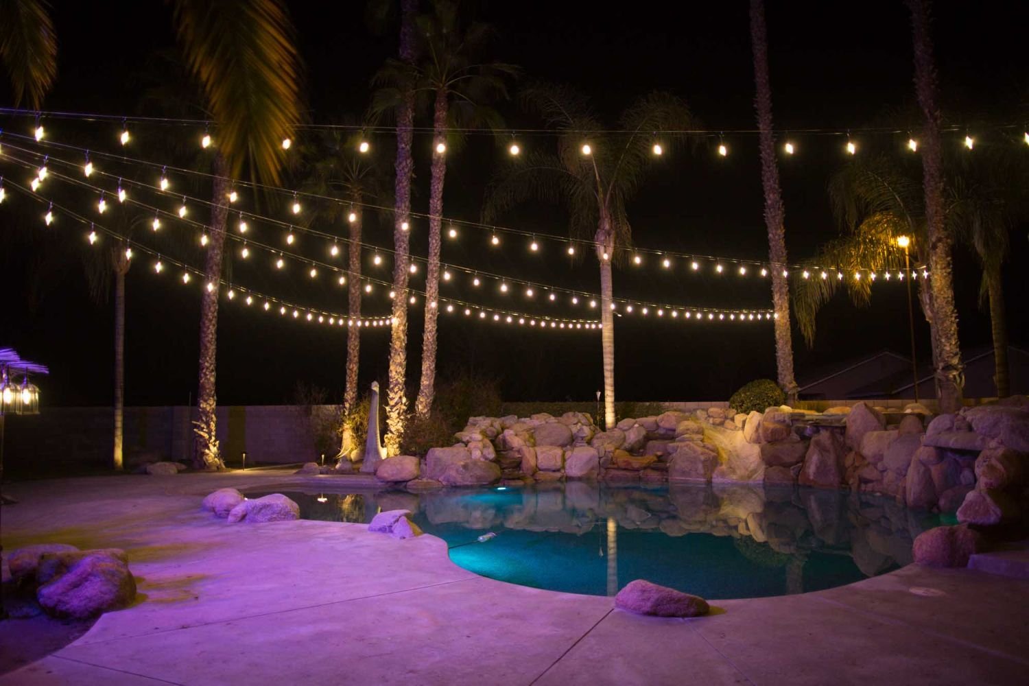 Warm string lights over palms and a Bakersfield pool at night