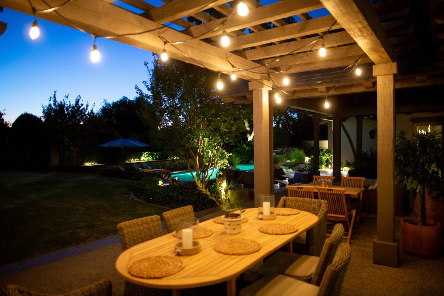 String lights over an outdoor pergola dining table beside a Bakersfield pool