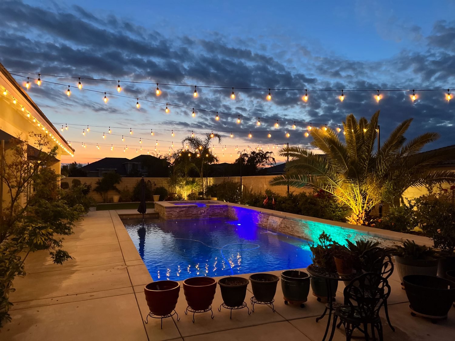 Outdoor string lights strung over a Bakersfield pool patio at sunset