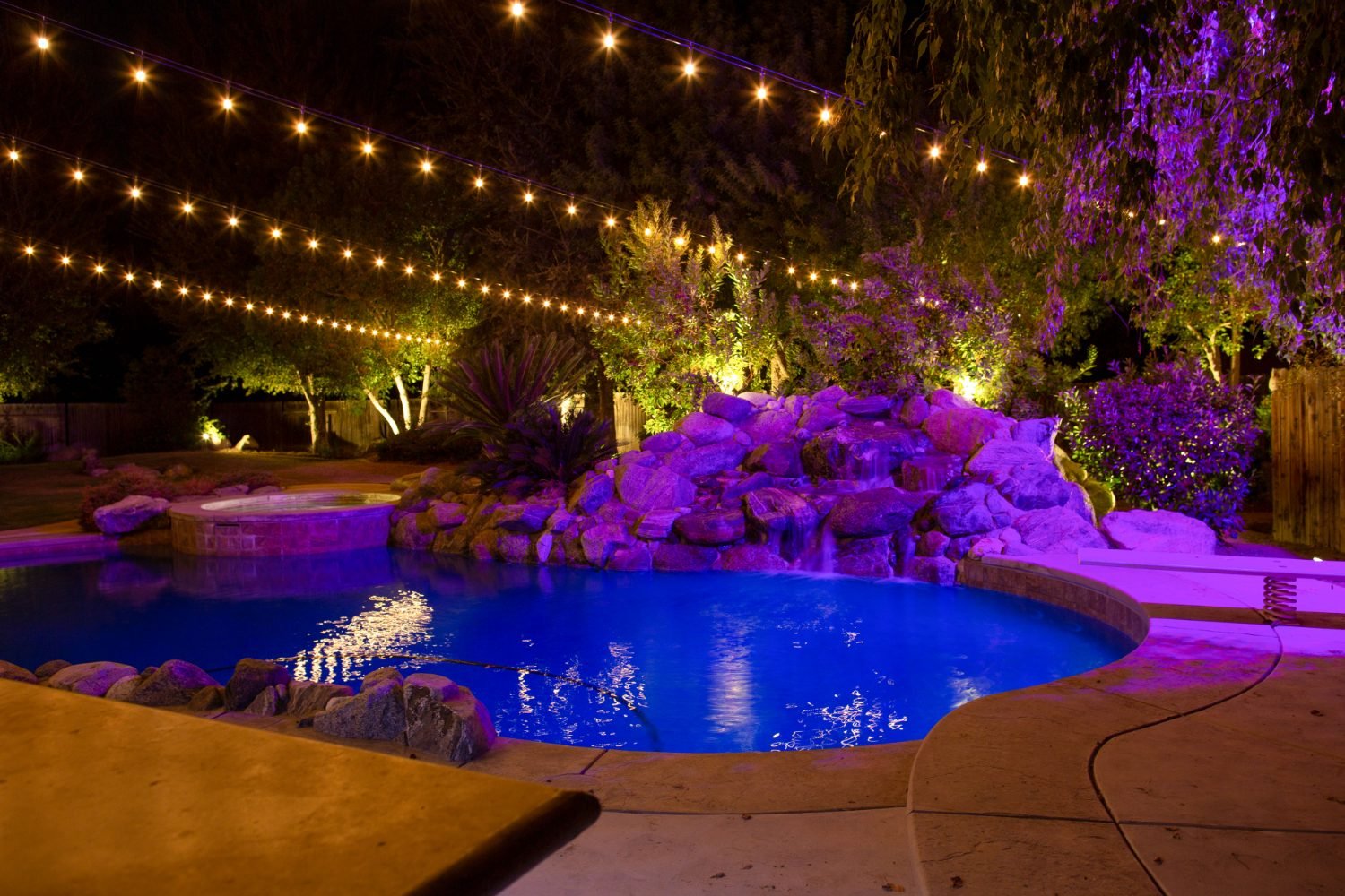 Outdoor string lights around a Bakersfield pool and waterfall at night